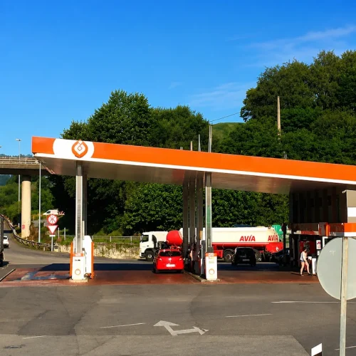 Fachada de gasolinera y amplio pavimento con árboles de fondo